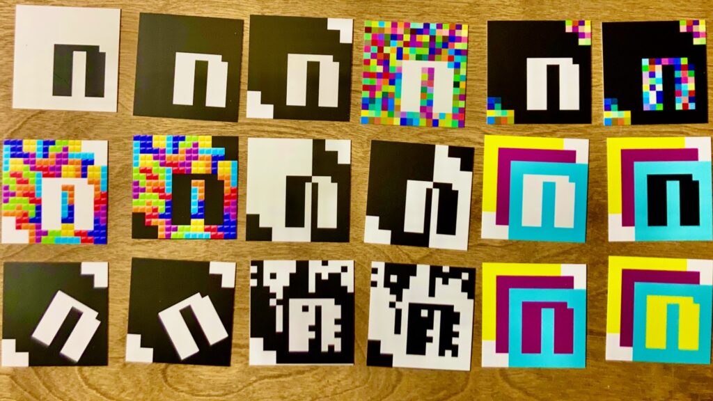 Backs of square Nudgital business cards showing various versions of the Nudgital logo, including black and white, Color Noise, Tetris, Lines, CMYK, SpinN, Rain, and Effervescence.